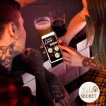 Couple tatoué utilisant le jeu coquins pour couple en format numérique au bar. Un ticket interactif pour couples audacieux.